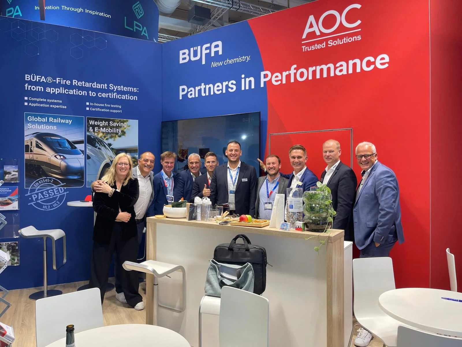 A group gathered at the B&Uuml;FA and AOC stand in front of the Partners in Performance banner.