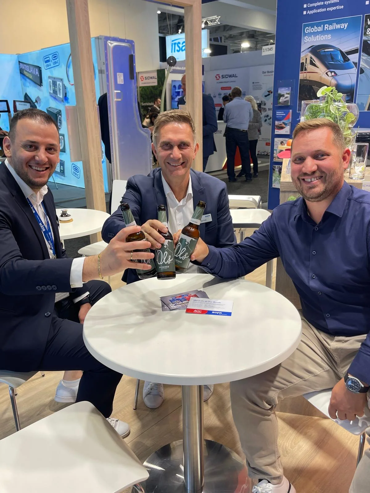 Three participants seated around a table at the B&Uuml;FA and AOC exhibition stand.