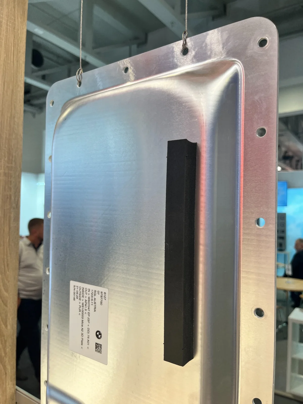 Close-up of the suspended composite battery top lid with its moulded surface and mounting holes.