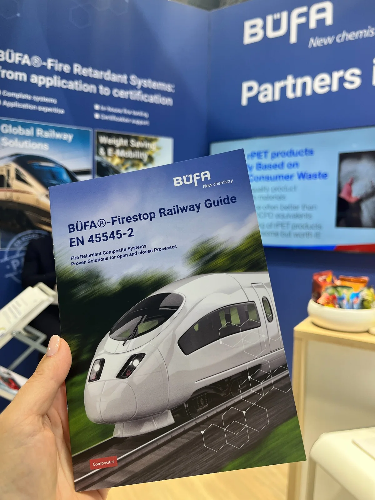 A hand holding the B&Uuml;FA Firestop Railway Guide brochure at the exhibition stand.