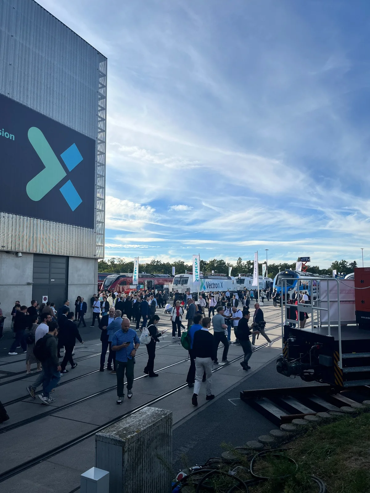 Visitors on the outdoor exhibition grounds at Messe Berlin under a blue sky.